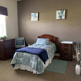 A cozy bedroom with a single bed, two dressers, and an armchair.