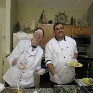 Two chefs smiling in a kitchen while preparing food.