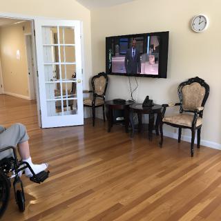A cozy living room with a television, chairs, and a person in a wheelchair on hardwood floors.