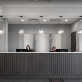 A modern office reception area with two staff members at the desk and stylish pendant lighting.