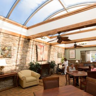 A cozy sunroom with natural light filtering through a glass ceiling, featuring comfortable seating and wooden tables, perfect for relaxation.