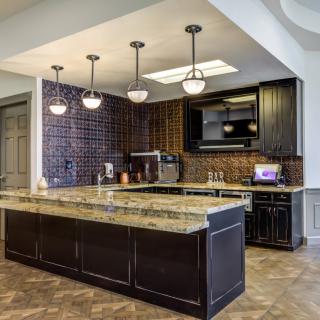 A modern kitchen with dark cabinets, granite countertops, and stylish lighting fixtures.