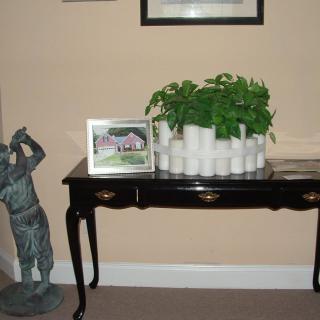 A decorative indoor setup featuring a table with a plant and photo frame, accompanied by a statue.