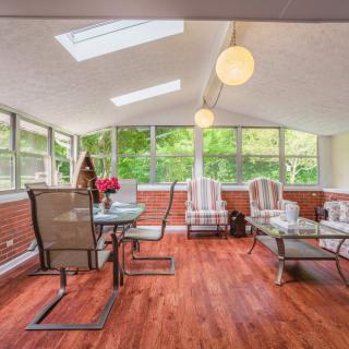 A bright sunroom with skylights, featuring a dining table and comfortable seating arrangements on a wood floor.