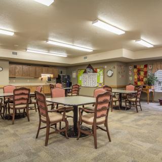 A spacious community dining room with tables and chairs, adjacent to a kitchen area.