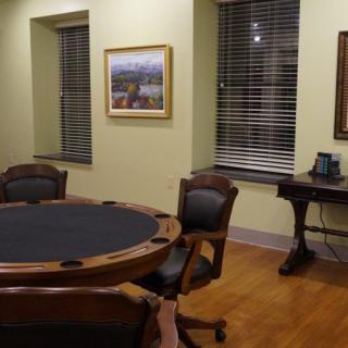 A cozy room with a round table and chairs, featuring artwork on the walls and large windows.