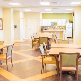 A bright and spacious communal dining area with tables and chairs, adjacent to a kitchen.