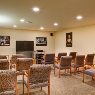 A cozy home theater room with seating arranged in rows facing a television, decorated with wall art and bright lighting.