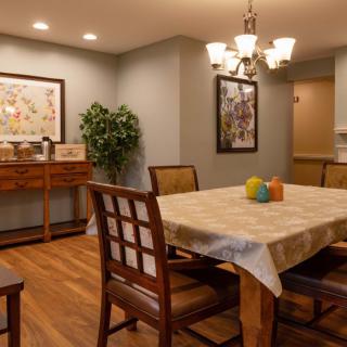A cozy dining room with a wooden table and chairs, decorated with artwork and a potted plant.