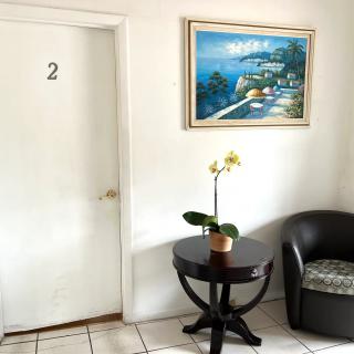 A waiting room with a chair, a table with a flower pot, and a painting on the wall near a door labeled '2'.
