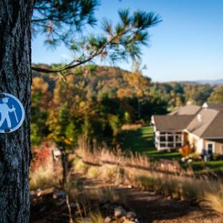 A picturesque view of a hiking trail sign on a tree, leading to a cozy home surrounded by autumn foliage.