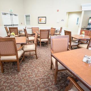A well-lit dining area with several tables and chairs arranged on a carpeted floor.