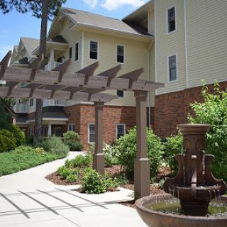 A beautifully landscaped outdoor area featuring a fountain and pathway leading to a modern building.