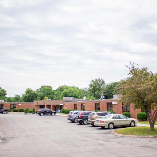 A view of a brick building with parked cars in a lot under a cloudy sky.