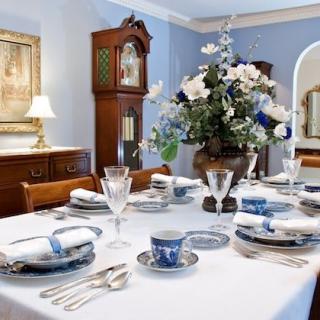 An elegantly set dining table featuring a blue and white theme, highlighted by fine china and a centerpiece of flowers.