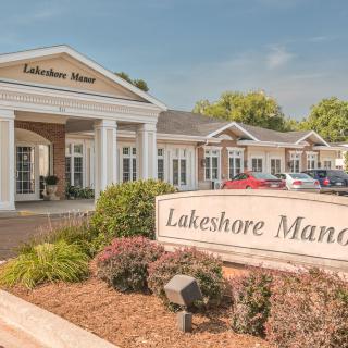 The image shows the entrance of Lakeshore Manor, featuring manicured landscaping and signage.