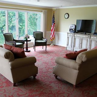 A cozy living room with sofas, chairs, a television, and an American flag near large windows.