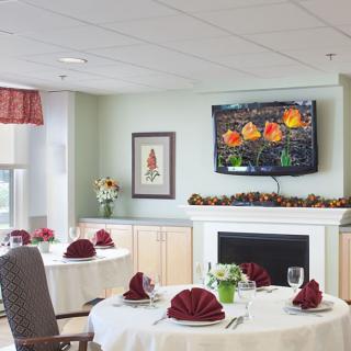 An elegantly decorated dining room with tables set, a television above the fireplace, and floral arrangements.
