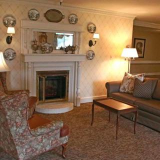 A traditionally styled living room featuring a cozy fireplace, seating area with a sofa and armchair, and decorative elements like wall-mounted plates and warm lighting.
