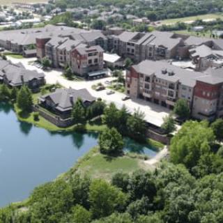 Aerial view of a residential apartment complex next to a scenic lake surrounded by trees.