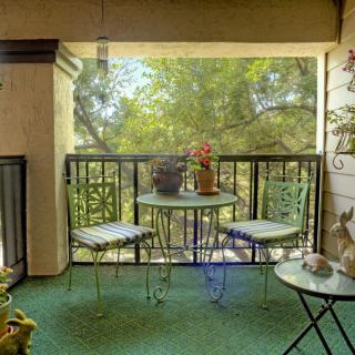 A cozy balcony setup with a small table, two chairs, and an array of plants overlooking lush greenery.