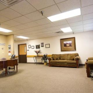 A spacious office waiting room with a comfortable sofa and chairs, illuminated by ceiling lights.