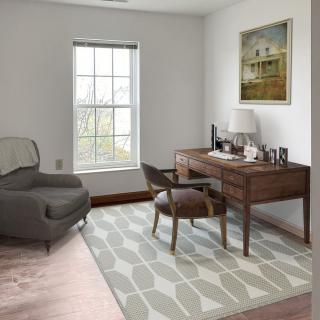 A cozy home office with a desk, chair, and armchair near a window.