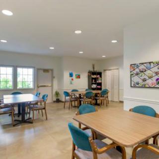 A spacious dining area with several tables and chairs, brightly lit by large windows and overhead lights, featuring artwork on the walls.