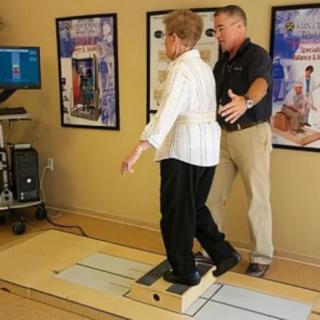 A therapist assists an elderly person during a balance training session using specialized equipment.