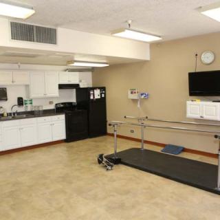 A physical therapy room equipped with parallel bars and a small kitchen area for rehabilitation exercises.