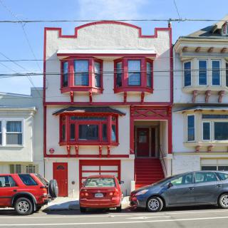 A vibrant red and white house in an urban neighborhood, flanked by parked cars along the street.