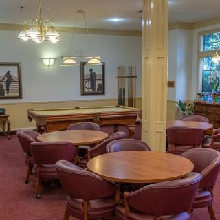 A cozy lounge area with round tables, leather chairs, and a pool table under elegant chandeliers.