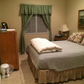 A cozy bedroom featuring a neatly made bed, warm curtains, and simple furnishings.