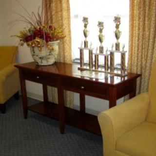 A wooden table displaying several trophies and a decorative vase with flowers, flanked by two yellow armchairs in a living room setting.