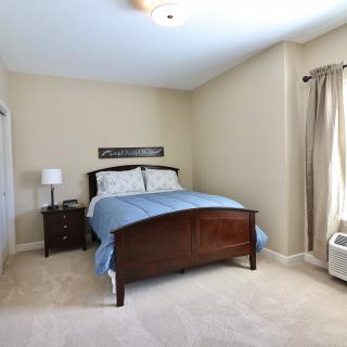 A neatly arranged bedroom with a wooden bed frame, blue bedding, and sheer curtains allowing light to fill the room.