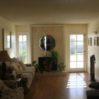 A cozy living room with a sofa, mirror above the fireplace, and natural light coming through doors and windows.
