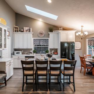 A modern kitchen with white cabinets, an island counter, and skylight, featuring an open concept design with a dining area.
