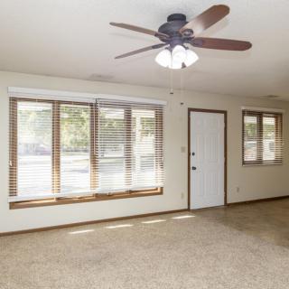 A spacious living room with large windows and a ceiling fan.