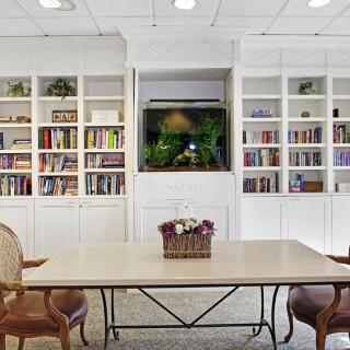 A cozy reading area with built-in bookshelves and a central table, complemented by an aquarium as a focal point.