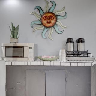 A small kitchen setup featuring a microwave, coffee makers, and decorative sun wall art.