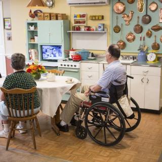 Two people sitting in a retro kitchen with vintage decor, watching television.
