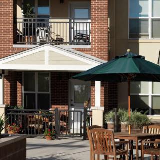 An inviting outdoor patio area with tables and an umbrella in front of an apartment building.