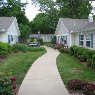 A curved pathway surrounded by gardens and leading to two houses.