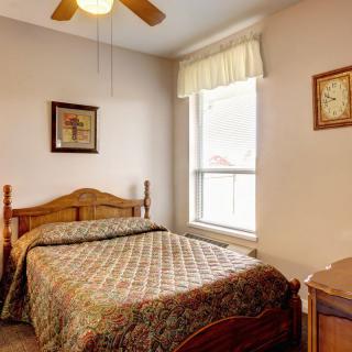 A cozy bedroom with a wooden bed, ceiling fan, and natural light coming through the window.
