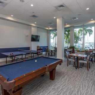 A modern game room featuring a pool table, tables, and chairs with natural light streaming through large windows.