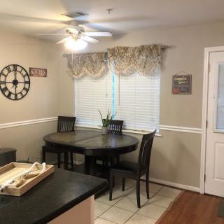 A cozy dining area with a round table, surrounded by chairs, under soft lighting and decorated with a wall clock.