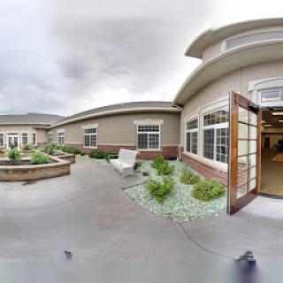 A serene outdoor courtyard featuring lush greenery and a modern architectural design, set against a cloudy sky.