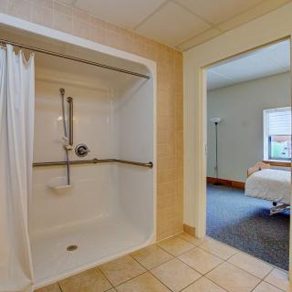 An accessible bathroom with a shower and curtain, featuring a grab bar, adjacent to a hotel room.