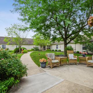 A serene outdoor patio area with comfortable seating surrounded by lush greenery and a well-maintained garden path.