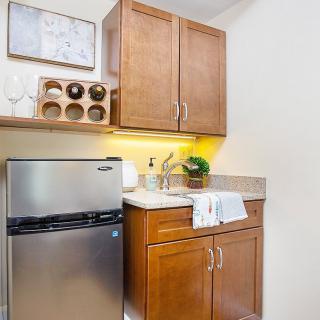 A compact kitchenette with a mini fridge, wood cabinets, and a small sink area.